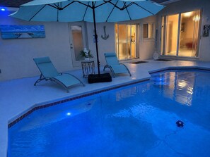 An indoor swimming pool with two lounge chairs and a table, a ceiling fan, and a large umbrella. - Tremendous 4-bedroom house with AC in charming Kissimmee (Kissimmee)