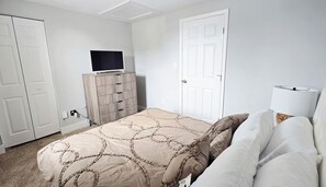 Quarto com cama, televisão sobre um móvel, porta e abajur.