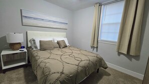 A bedroom with a bed, nightstand, lamp, and a painting on the wall.