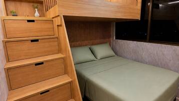 Uma cama beliche com escada de madeira que dá acesso a um espaço de estudo com gavetas e uma pequena planta.