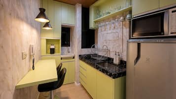 Cozinha compacta com micro-ondas, pia e banquetas de bar.
