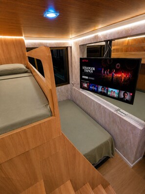 Een kleine kamer met een bed, een aan de muur bevestigde televisie en een raam.