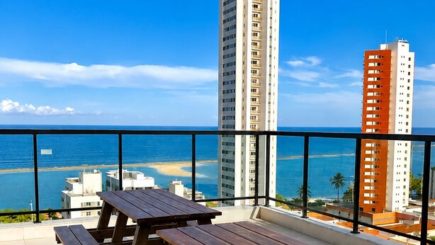 A balcony with picnic tables overlooking a beach and ocean. - Premium Apartment in Olinda | Swimming Pool, Gym, and Panoramic Ocean Views (Recife)