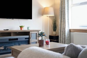 A living room with a flat-screen TV mounted on the wall, a coffee table with a plant and a jar, a sofa, and a floor lamp. - Easy Edinburgh Access, Parking,Near Rosslyn Chapel (Midlothian)