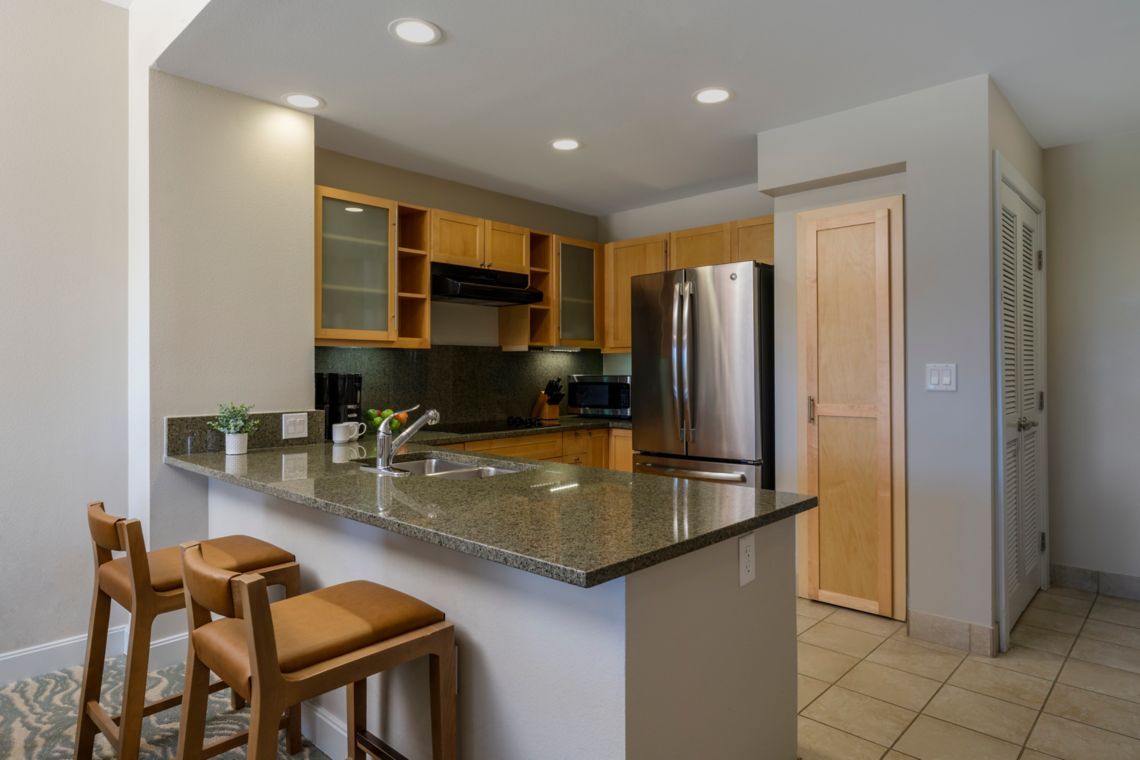 Una cocina moderna con encimeras de granito, electrodomésticos de acero inoxidable, armarios de madera y una isla integrada con taburetes de bar.