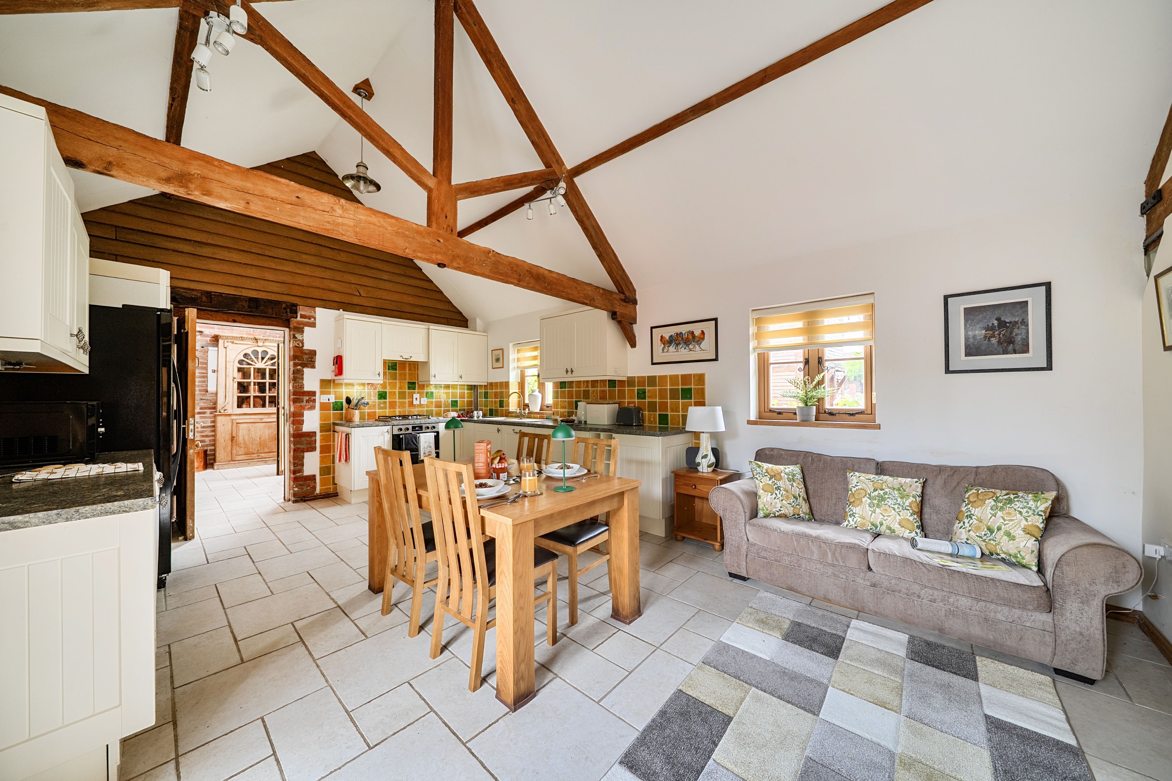 Uma cozinha espaçosa com vigas de madeira, uma sala de jantar com mesa e cadeiras, e uma sala de estar com sofá e almofadas.