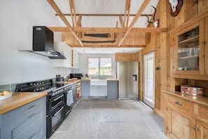 A kitchen with a stove, oven, and refrigerator, wooden cabinets, and a window.