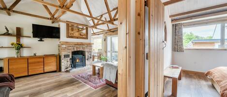 A spacious room with a wooden ceiling, a fireplace, a television, and a large window.
