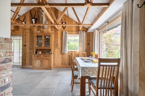 A rustic wooden interior with a dining area, stone flooring, and a view through large windows.
