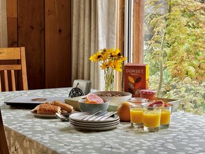Een ontbijttafel met gebak, een kom cornflakes, een vaas bloemen, een doos muesli en glazen jus d'orange.
