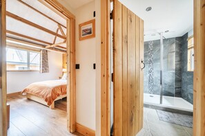 A bedroom with a bed, a window, and a door leading to a shower area with a glass door.