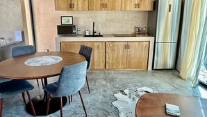 Cozinha moderna com armários de madeira, geladeira de aço inoxidável e área de jantar com mesa e cadeiras de mármore.
