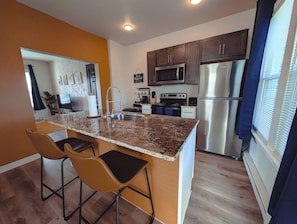 A modern kitchen with granite countertops, stainless steel appliances, and a bar stool seating area. - Historic Detroit Charm • 10 min Downtown (Detroit)