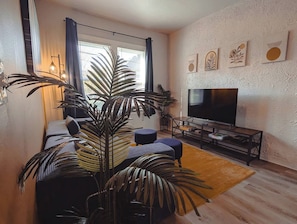 A modern living room with a large flat-screen TV, a sofa, a coffee table, and a potted plant. - Historic Detroit Charm • 10 min Downtown (Detroit)