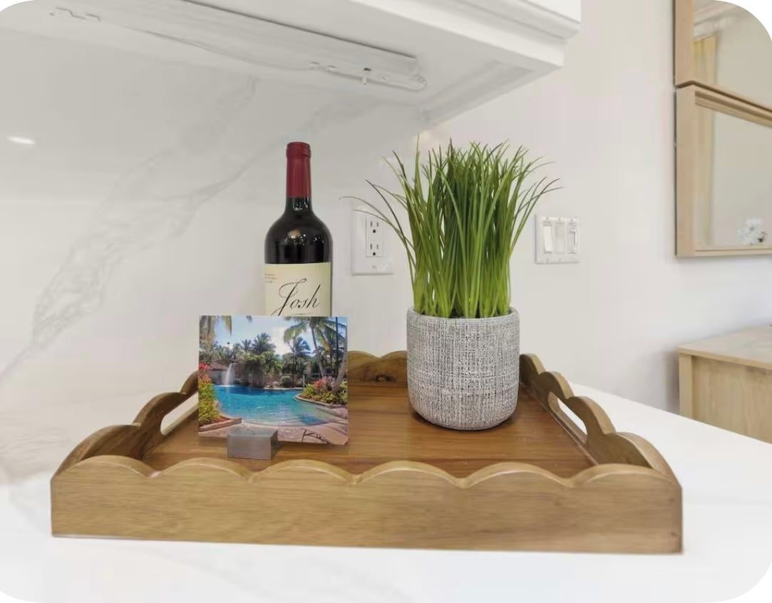 A wooden tray with a bottle of wine, a card, and a potted plant on a white surface.