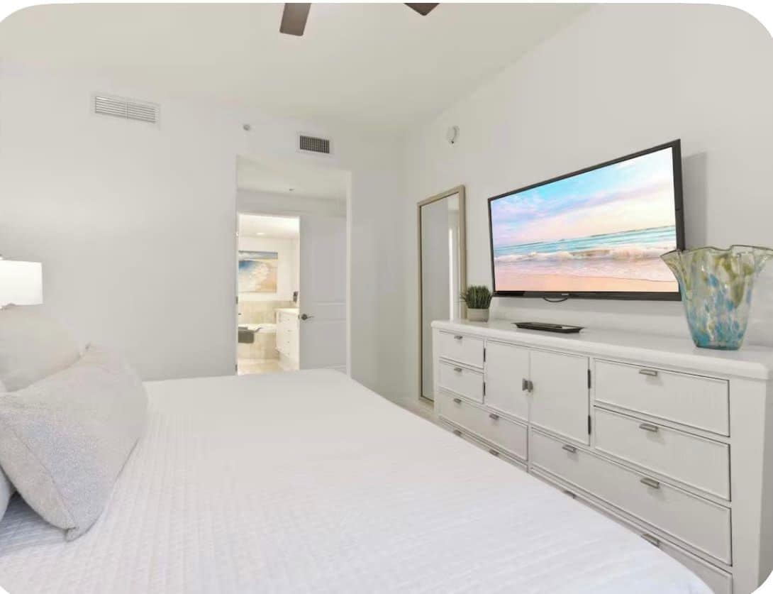 A bedroom with a bed, a television on a dresser, and a vase on the dresser.