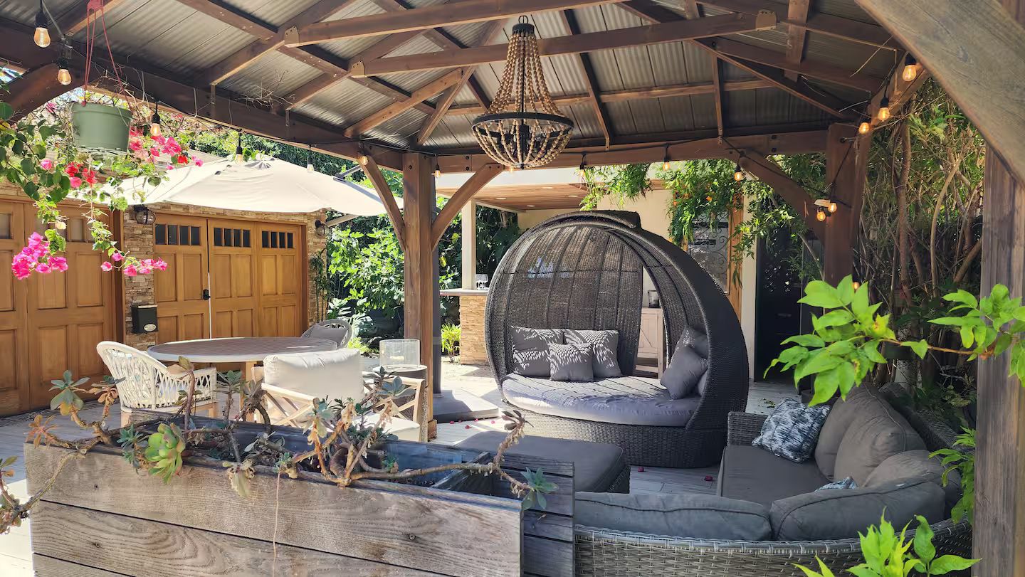 An outdoor patio with a wooden pergola, wicker furniture, hanging plants, and a hanging light fixture.