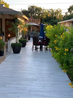 Ein Außenbereich mit Terrasse, Tisch und Stühlen, umgeben von Blumentöpfen und einem Weg.