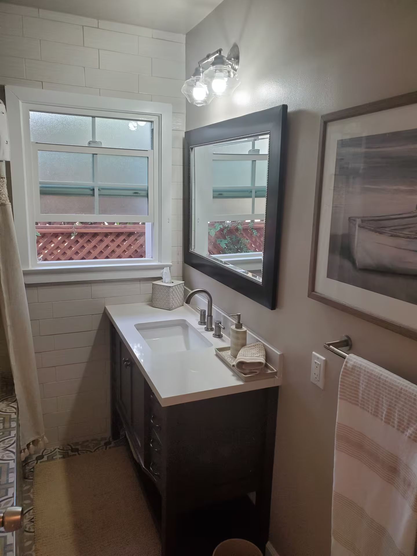 Une salle de bain avec un lavabo blanc, un meuble-lavabo foncé, une fenêtre donnant sur un beau paysage et un miroir.