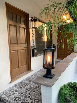 A wooden door with a mailbox and a number plate, a lit lantern, and a potted plant. - Bright and Cozy Retreat near Sony Studios (Culver City)
