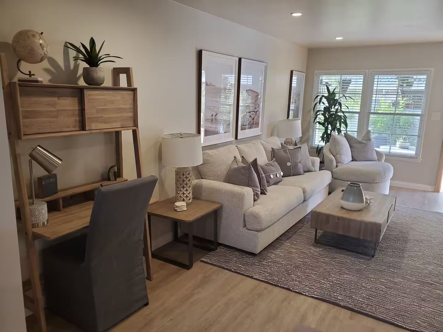 Uma sala de estar moderna com sofá, mesa de centro e mesa lateral. Há quadros nas paredes, um vaso de planta e um abajur sobre a mesa lateral.