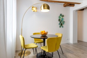 Een eetgedeelte met een ronde tafel, gele stoelen, een gouden vloerlamp en een schaal fruit.