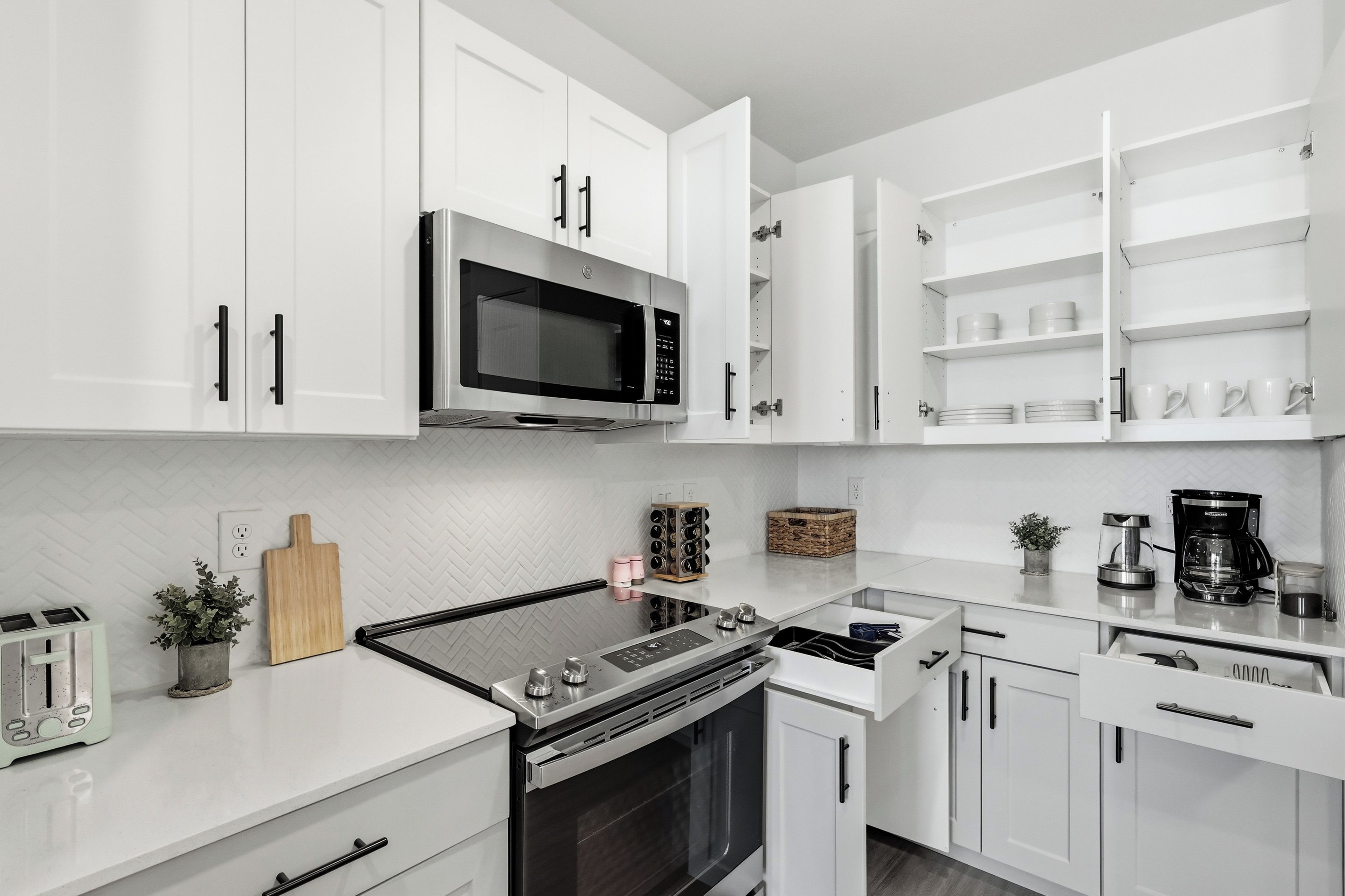 Une cuisine moderne avec des meubles blancs, un four à micro-ondes encastré, une cuisinière et une machine à café.