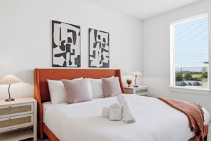 Un dormitorio moderno con una cama grande, dos mesitas de noche, una ventana con persianas y arte abstracto en la pared.