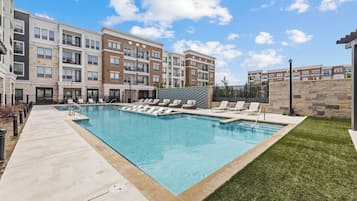 Un immeuble d’appartements moderne doté d’une piscine et de chaises longues.
