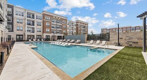 Un edificio de apartamentos moderno con piscina y sillones de descanso.