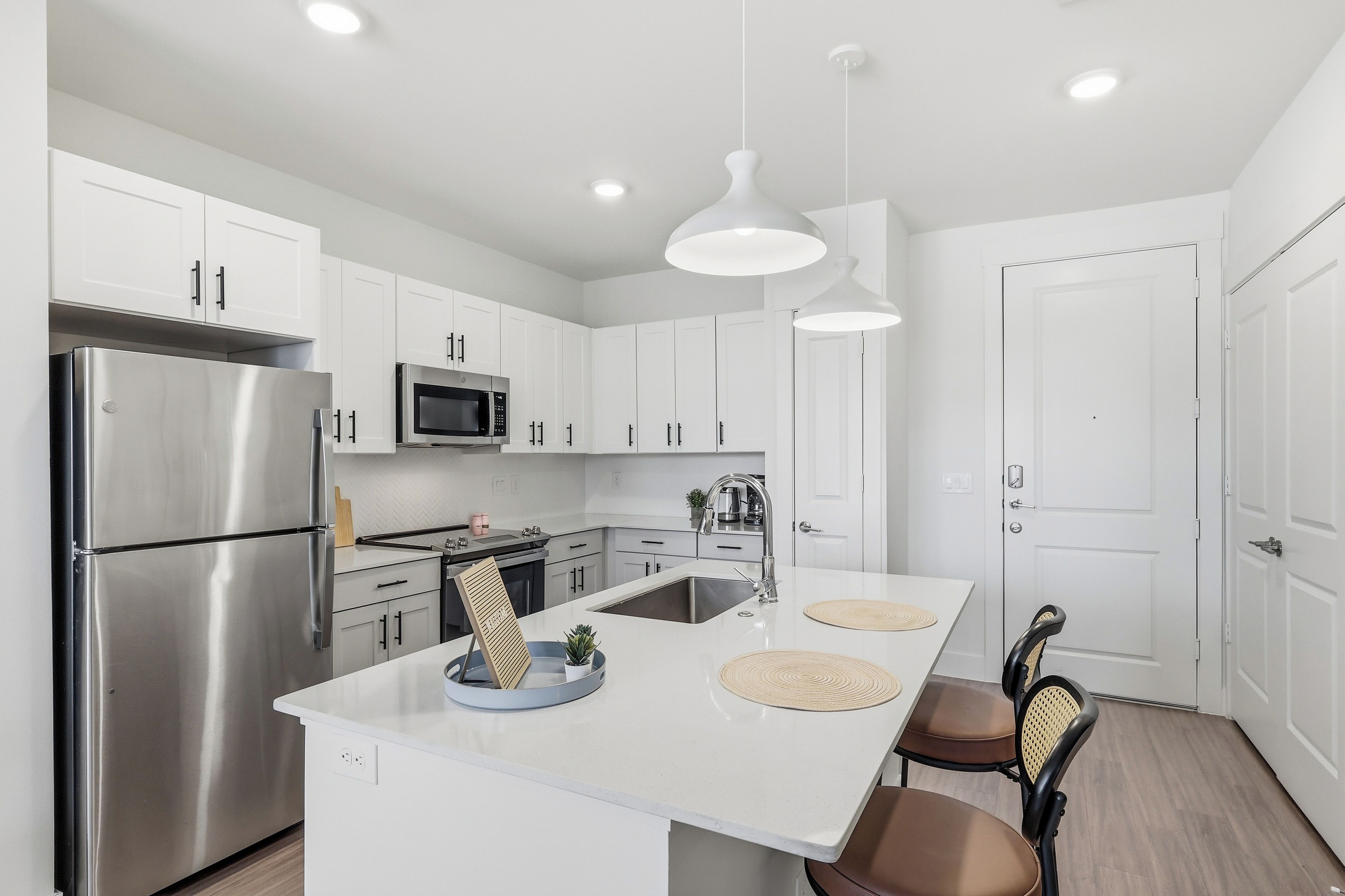 A modern kitchen with white cabinets, stainless steel appliances, and pendant lighting.
