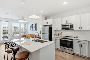 Una cocina moderna con armarios blancos, electrodomésticos de acero inoxidable y una isla central con taburetes.