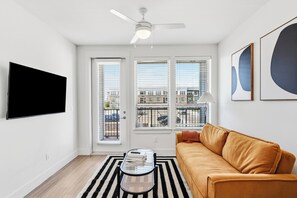 Una sala de estar moderna con un sofá, una mesa de centro, un televisor montado en la pared y un ventilador de techo.