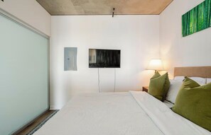 A bedroom with a bed, a television mounted on the wall, a bedside lamp, and a green wall art piece. - Waterfront View 1bdrm Downtown, Free Parking, Next to Pier, Pike Place and Lumen (Seattle)