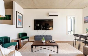 A living room with a flat-screen TV mounted on the wall, a coffee table, and seating including a sofa and chairs. - Waterfront View 1bdrm Downtown, Free Parking, Next to Pier, Pike Place and Lumen (Seattle)