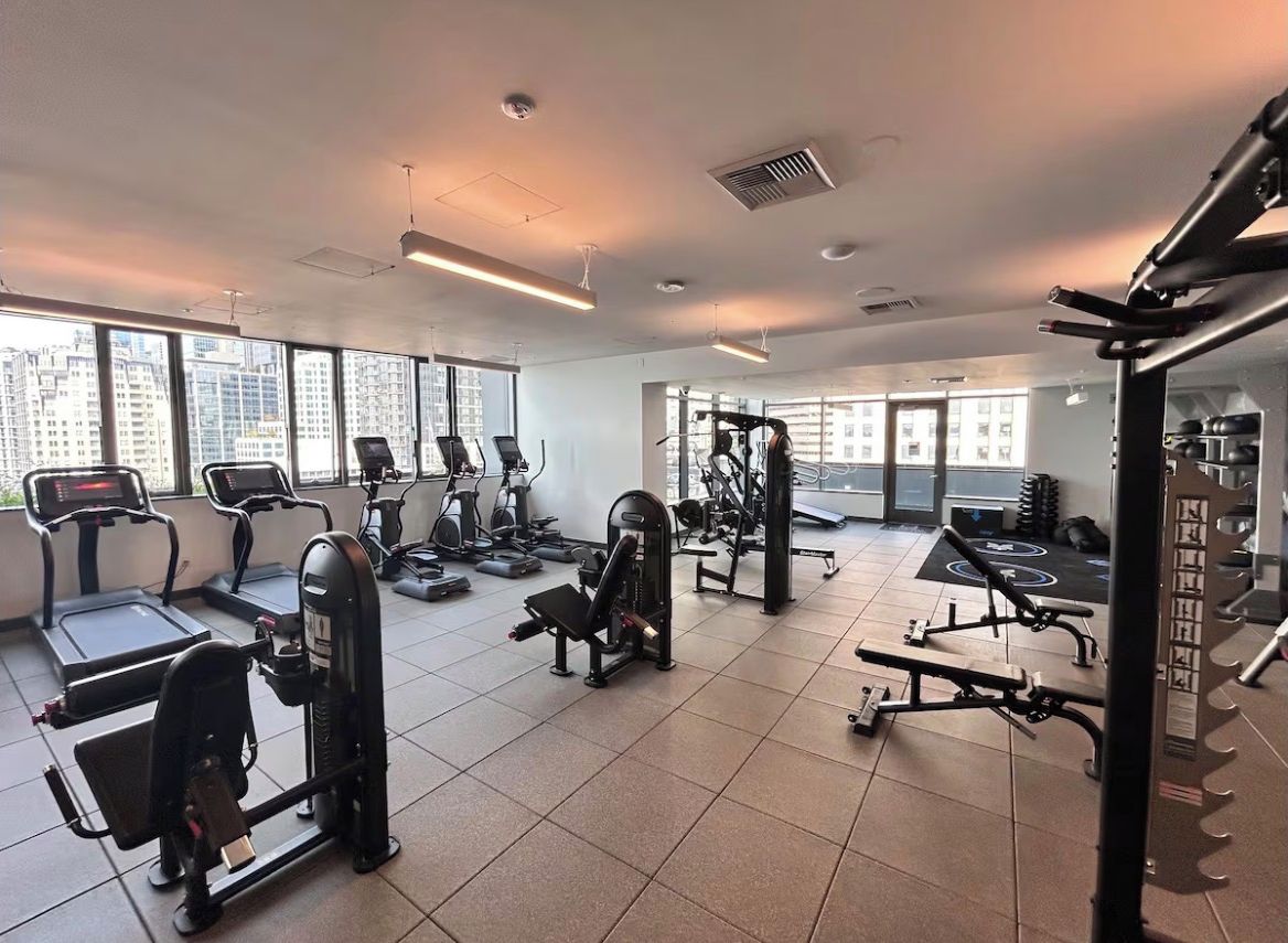 A gym with exercise equipment, large windows, and a view of buildings.