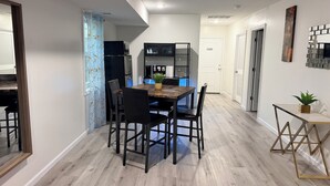 A dining area with a wooden table and chairs, a kitchen with a refrigerator and cabinets, and a hallway with a door.
