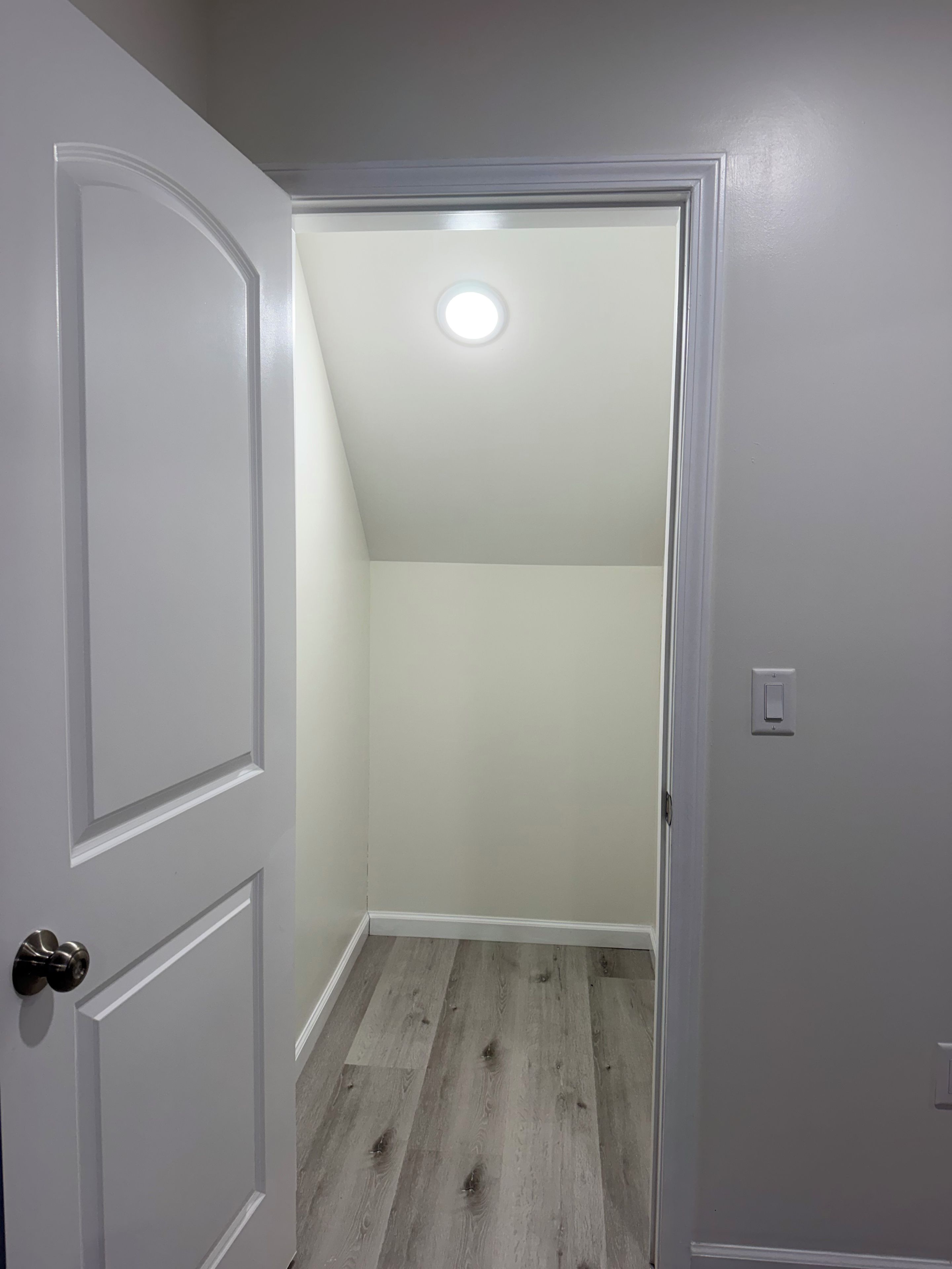 Un corridoio con una porta bianca che conduce a una stanza con soffitto spiovente e un lampadario.