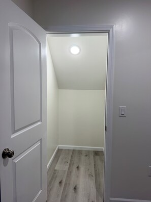 A hallway with a white door leading to a room with a sloped ceiling and a light fixture.