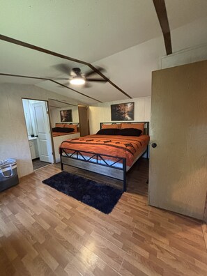 A bedroom with a bed, a ceiling fan, a door, and a small bathroom. - Welcoming 2-bedroom mobile home with peaceful setting (Eucha)