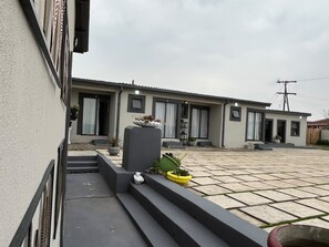 Un edificio residencial con un patio empedrado, un pequeño jardín con plantas en macetas y una entrada visible.