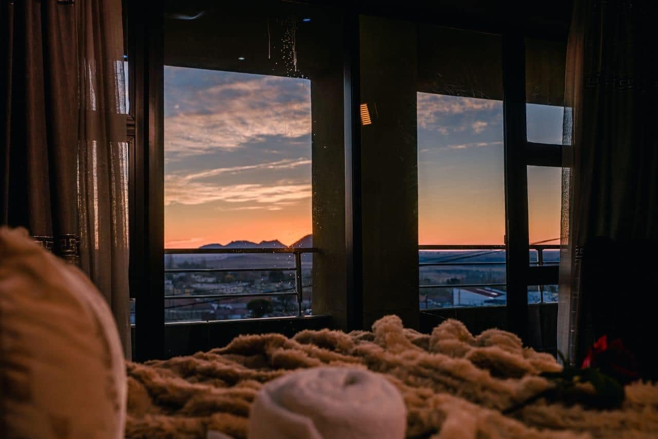 A room with a large window overlooking a cityscape at sunset.
