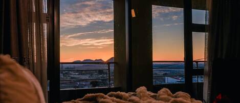 A room with a large window overlooking a cityscape at sunset.