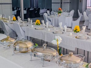 Un salón de banquetes con mesas dispuestas para un evento formal, con cubertería, platos y cristalería.
