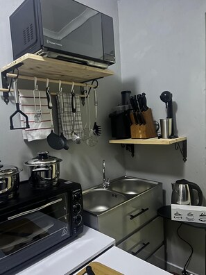 A compact kitchen with a microwave, stove, sink, and various utensils.