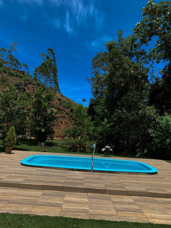 Ein Swimmingpool unter blauem Himmel, umgeben von üppiger Vegetation und Bäumen.