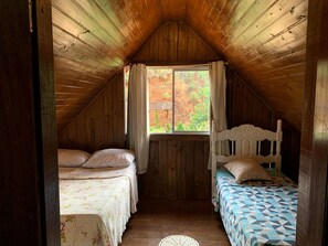 Ein kleines, gemütliches Schlafzimmer im Dachgeschoss mit zwei Betten, Holzwänden und einem Fenster mit Vorhängen.