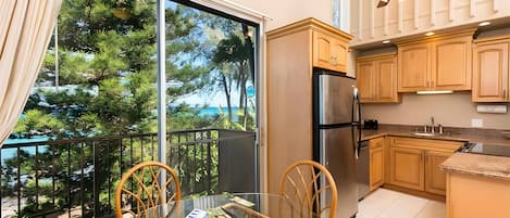 Una cocina con refrigerador, armarios de madera y un comedor con mesa y sillas de vidrio.
