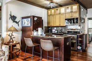 A kitchen with wooden cabinets, a central island with bar stools, a coffee maker, and a microwave. - Kahana, Polynesian Shores, Spacious 4 BR, Beachfront, Sleeps 12 (Lahaina)