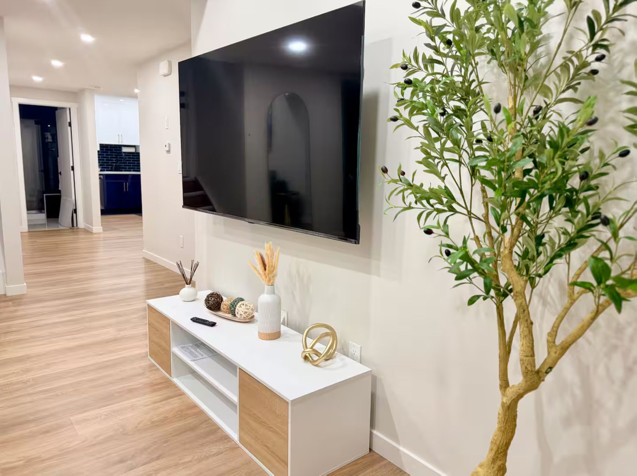 Una sala de estar moderna con un televisor de pantalla plana montado en la pared, una consola blanca con objetos decorativos y una planta en maceta.